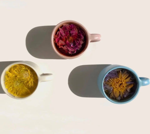 different colored mugs containing whole flower chrysanthemum tea, whole flower rose tea, and whole flower blue lotus tea