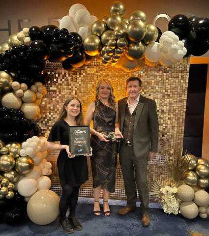 The Hotham's Team at the HullBID Awards 2023, stood holding the award, next to a balloon wall, gold black and white balloons