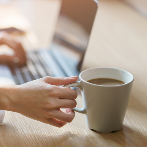 person's hand holding on a coffee cup while on their computer working on laptop