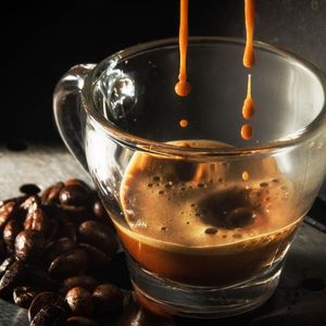 close-up of espresso coffee dripping into a cup next to whole dark coffee beans