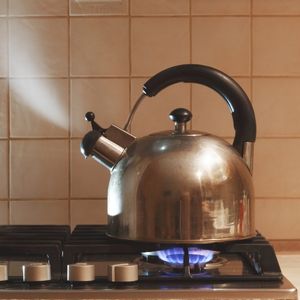 a kettle on top of a lit gas stove with steam pouring out of the kettle