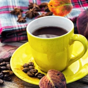 a yellow mug of coffee surrounded by fall leaves, coffee beans, and spices