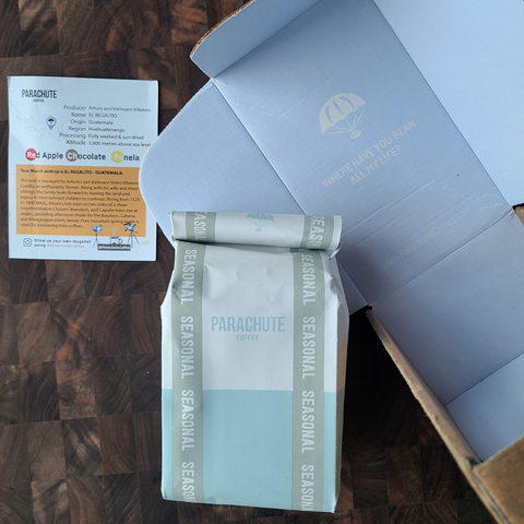a bag of parachute coffee next to a delivery box and post card