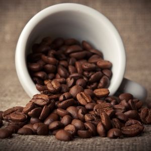 Side view of a mug lying on its side with whole roasted coffee beans spilling out of it to show why buy fresh roasted coffee