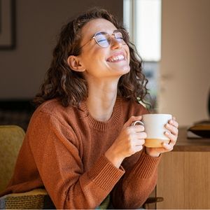 a bespectacled woman smiling while holding a mug of coffee