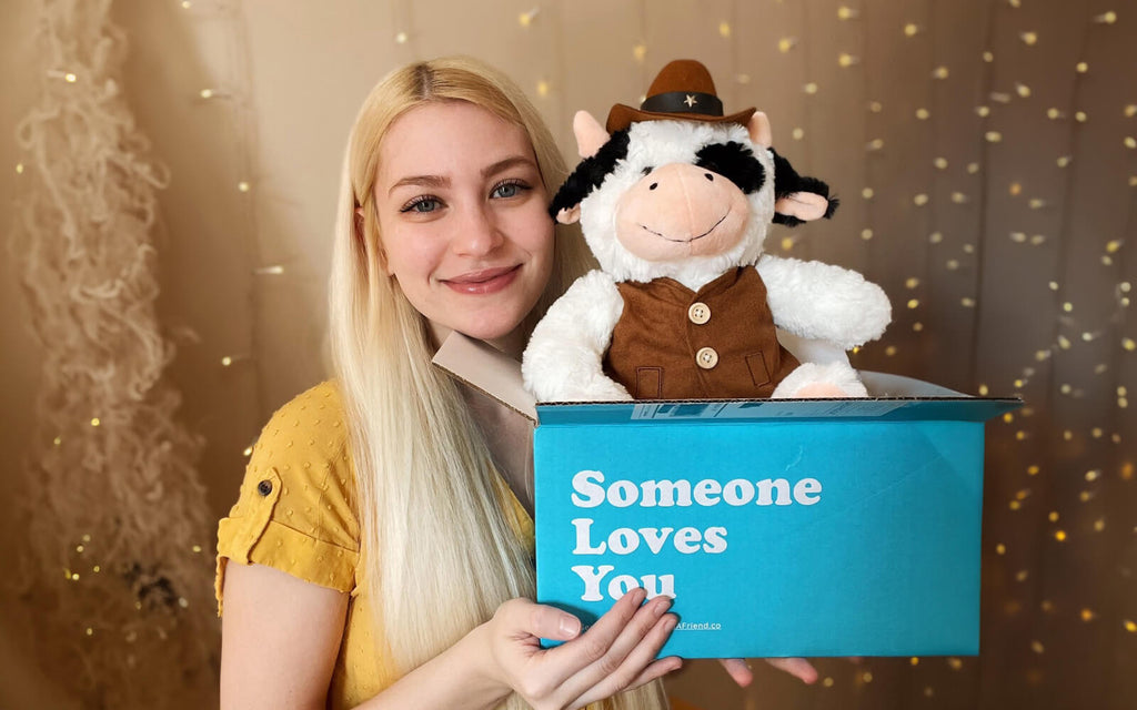 woman holding a stuffed animal cow dressed as a cowboy in a "someone loves you" box