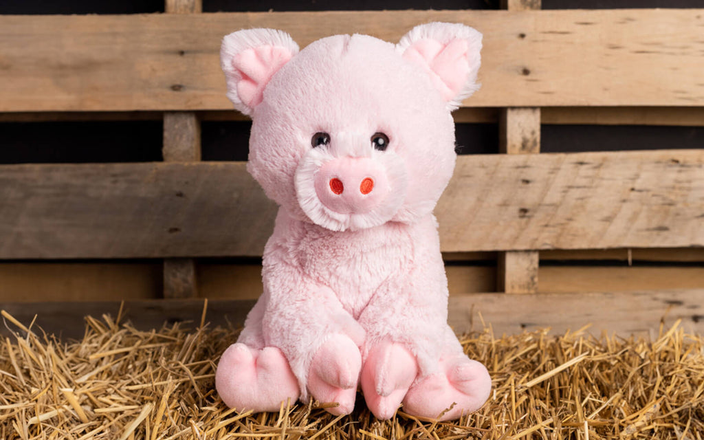 stuffed animal pig sitting on straw with wood background