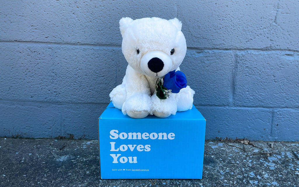 Pictured is Peaches the Polar Bear sitting on a "Someone Loves You" box holding a Blue Rose