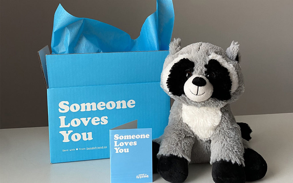 Photo of Rosie the Raccoon sitting with open Someone Loves You box and note card