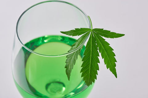 Close-up on a glass of weed wine with a hemp leaf on gray background