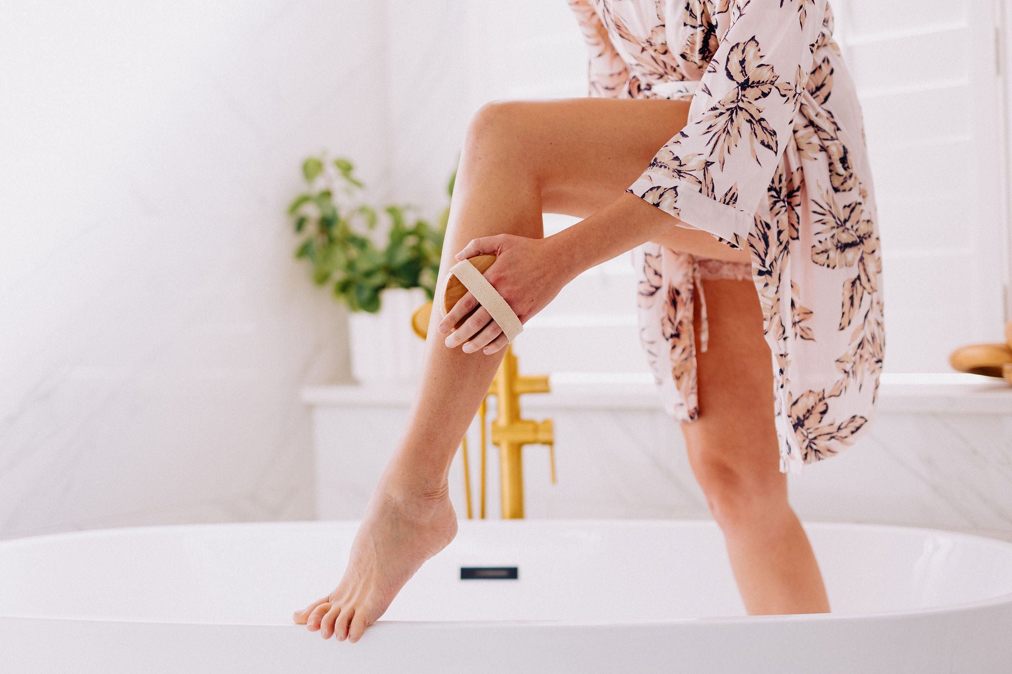 woman using body brush on her upper thigh in her bathroom
