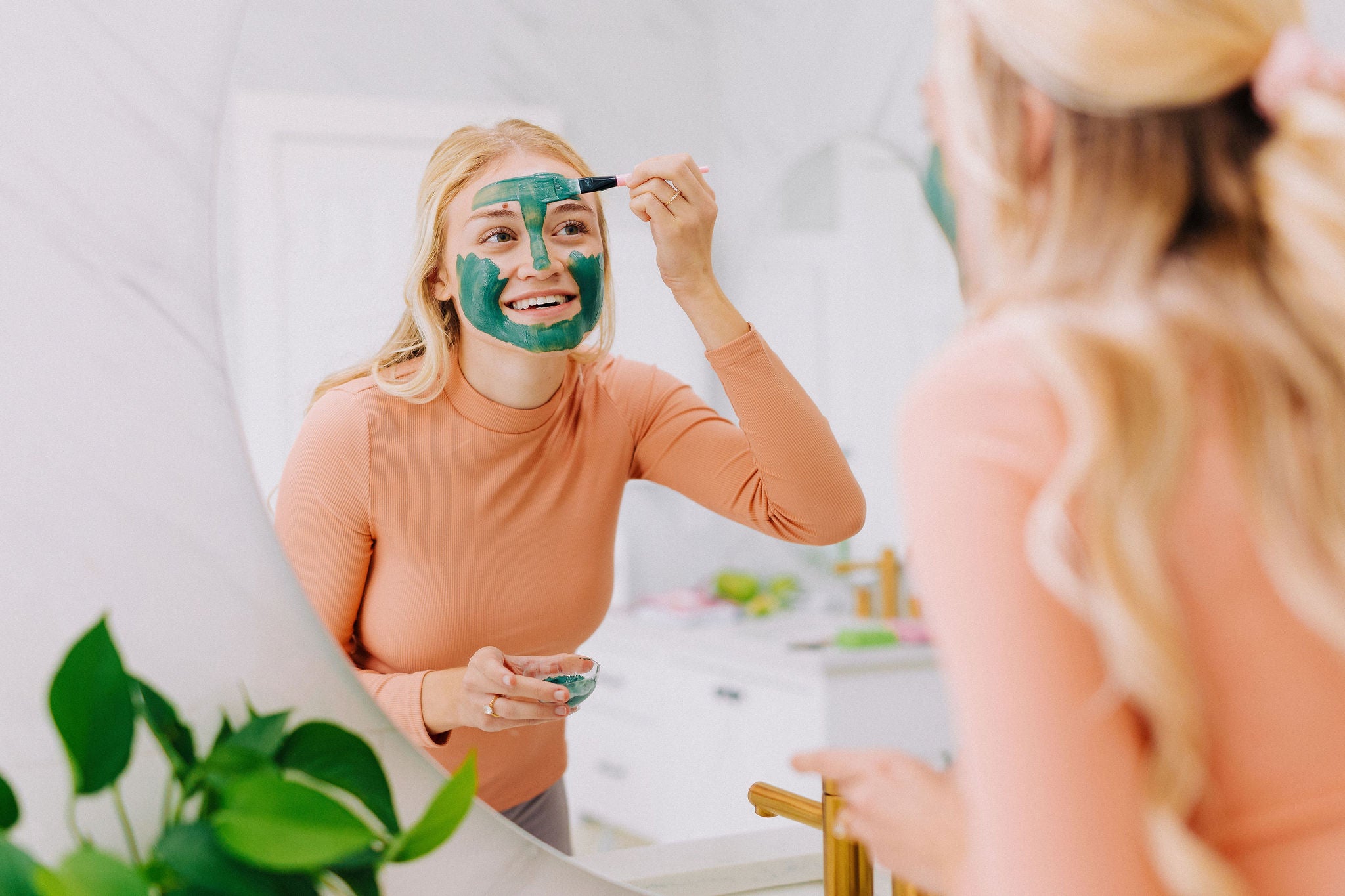 woman looking in the mirror applying clay mask