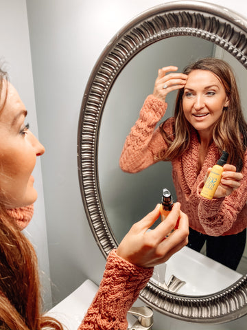 woman looking in mirror applying skin serum with vitamin c to forehead