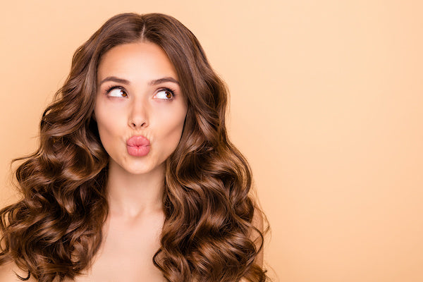 woman with long brown wavy hair pursing lips as if giving a kiss