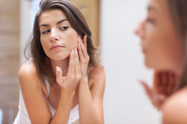 woman looking in mirror touching her face inspecting for acne breakouts