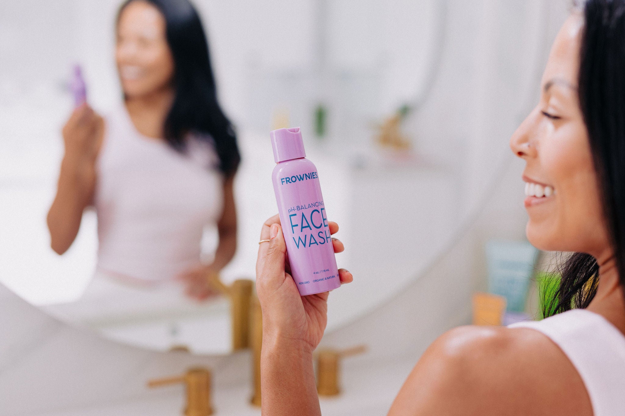 woman holding pH balancing face wash in front of the mirror