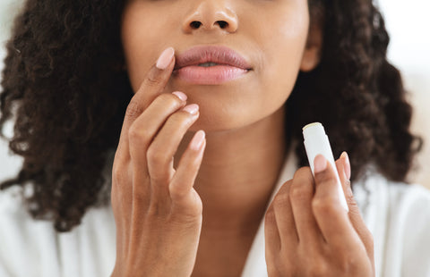 woman holding white tube of lip balm applying to lips with her finger