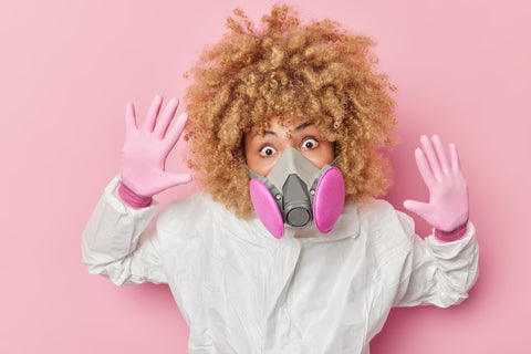 woman with short, curly, blonde hair wearing white lab coat and pink gloves and pink gas mask