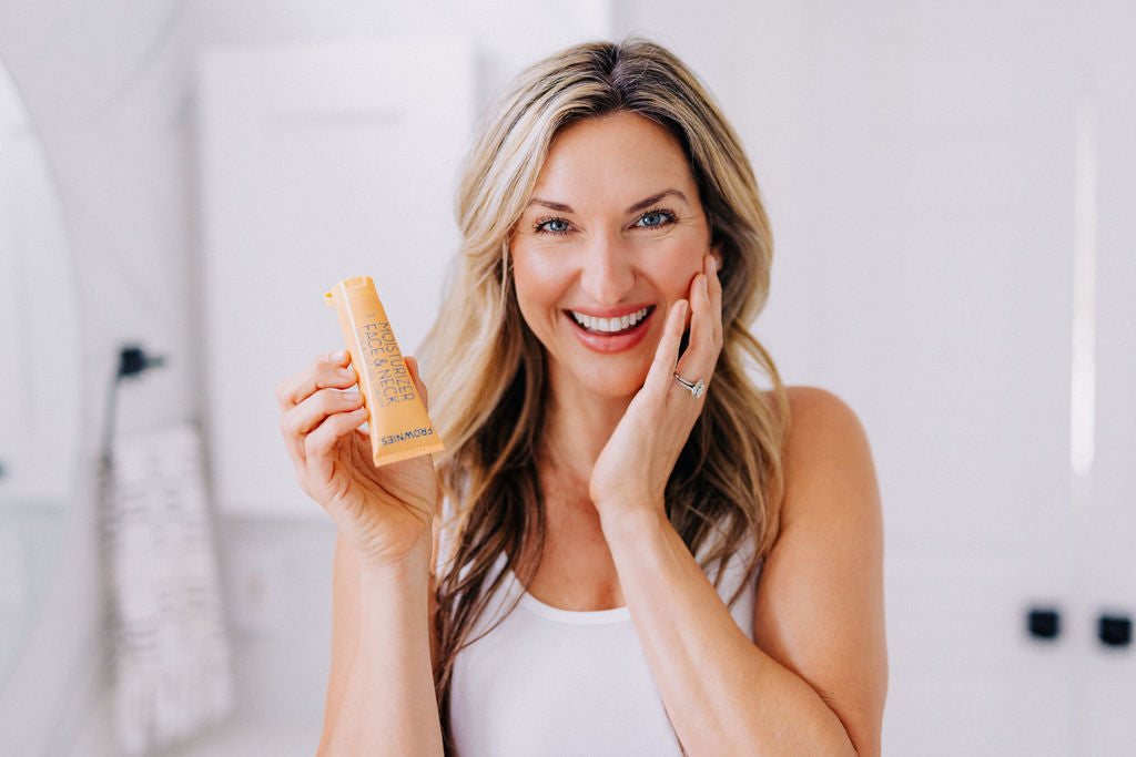 woman holding face moisturizer touching her cheek