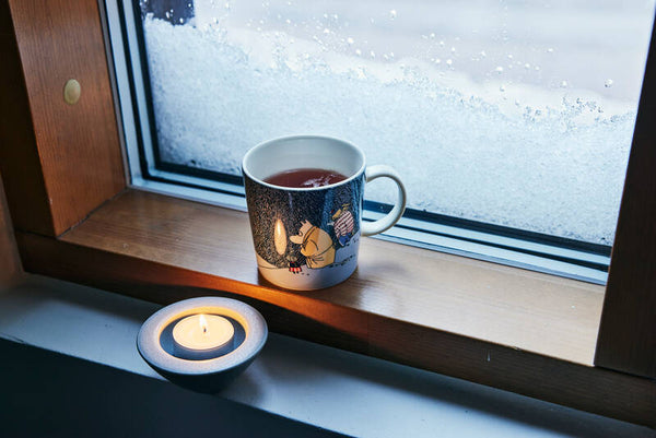 Zaubert eine gemütliche Stimmung: Der Moomin-Winterbecher 2021 Snow Moonlight und ein Teelicht. 