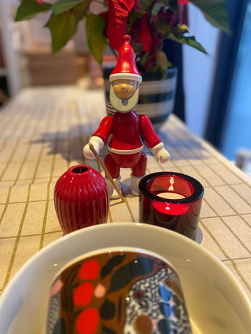 Damit es auf dem Tisch schön weihnachtlich wirkt, stehen Kivi-Windlicht von iittala und Hammershoi-Vase mini von Kähler in rot bereit. Der Weihnachtsmann von Kai Bojesen rundet mit dem Weihnachtsstern im Hintergrund im Omaggio Übertopf in grün das Ensemble ab. 