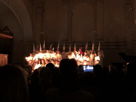 Lucia Konzert mit Lichtern und Stjärngossar, Männern im Chor mit spitzen Hüten.