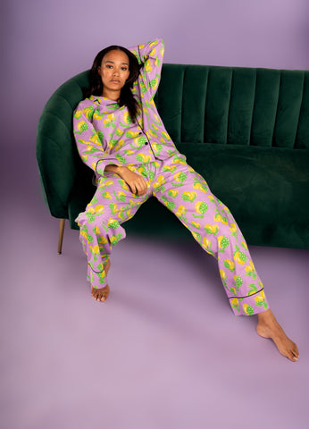A close-up of a woman wearing loose-fitting lemon-print pajamas, lounging comfortably on a sofa with a book in hand. The pajamas feature a relaxed fit and are made from breathable cotton fabric, promising luxurious comfort for both sleep and lounging. The image showcases the versatility of the pajamas, suggesting they can be styled for both lazy days indoors and chic outings with statement accessories and sleek footwear.