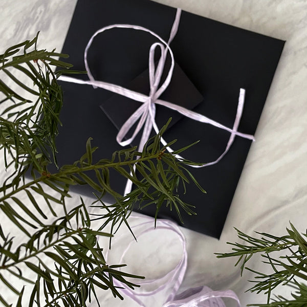 A square gift wrapped in black wrapping paper, with a lilac raffia bow.