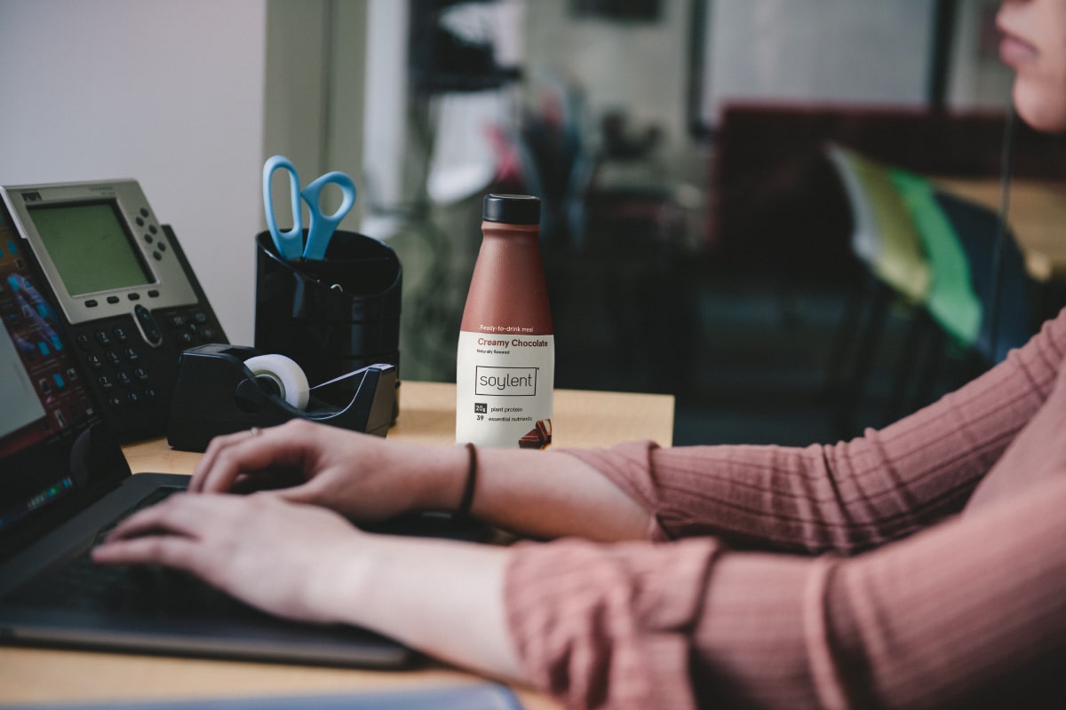 Image of a person sitting at a desk beside a bottle of Chocolate Soylent