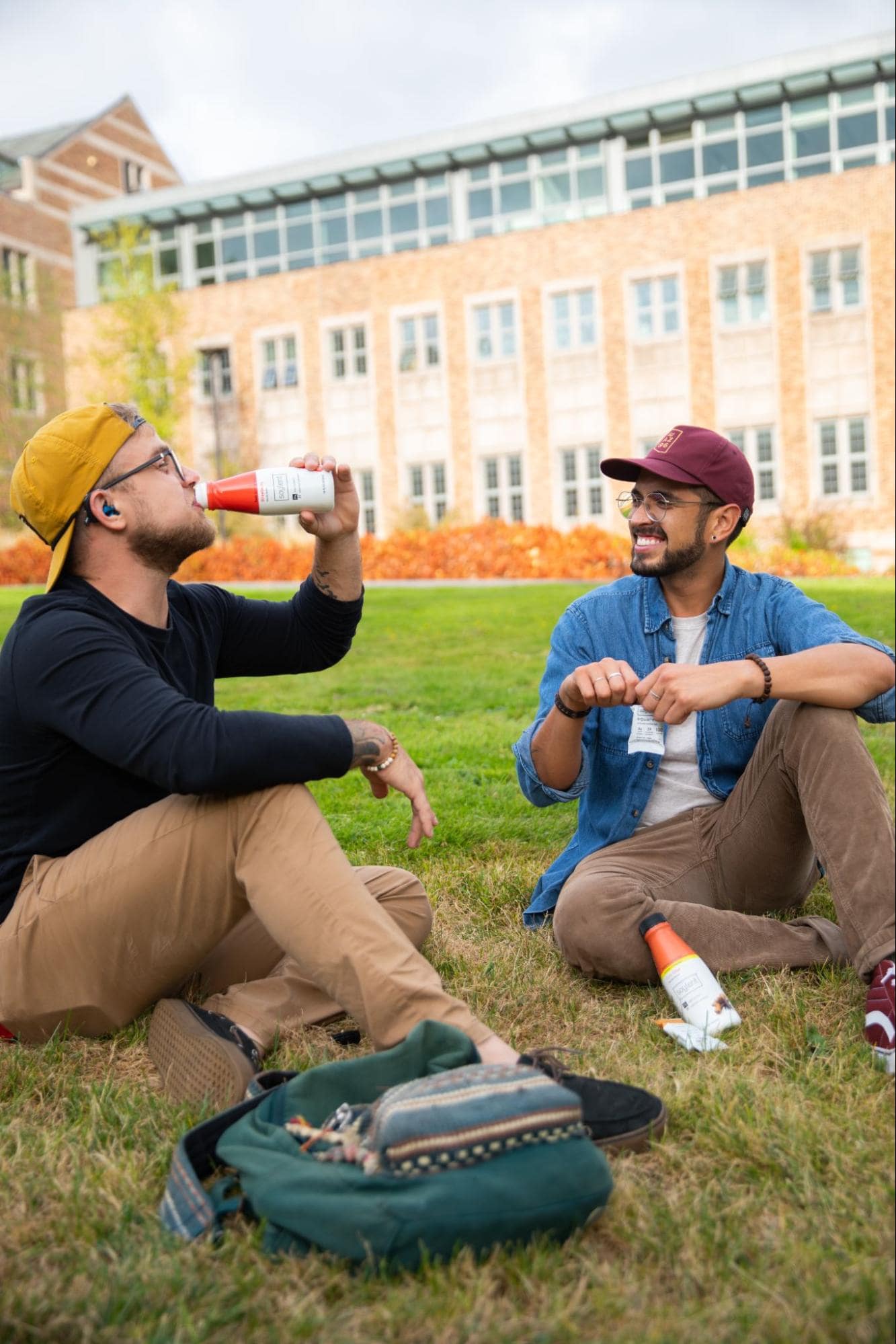 Image of two people sitting on a lawn, drinking Soylent