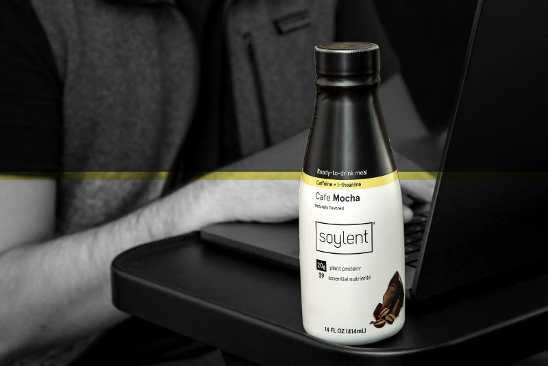 Bottle of Soylent complete coffee in cafe mocha on desk near laptop.