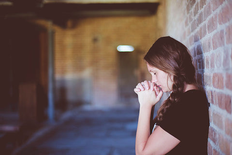 woman praying against a brick wall