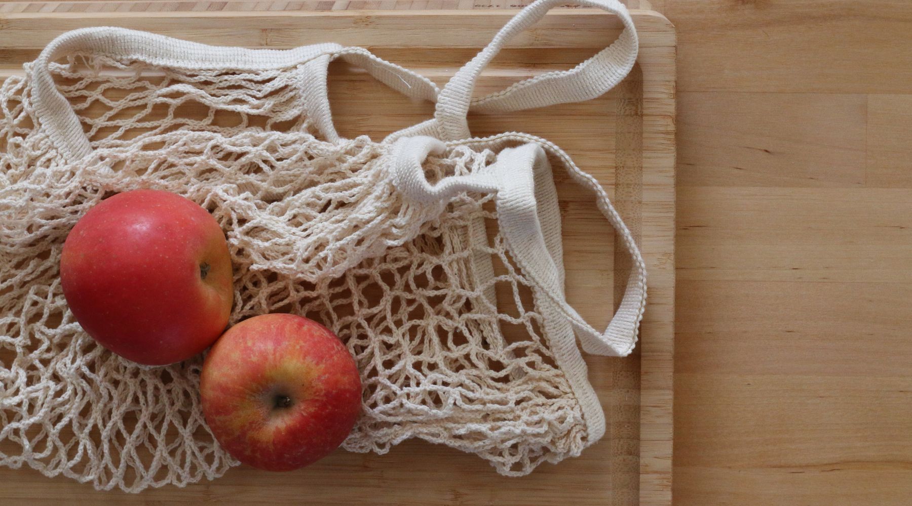 Mesh reusable bag laying on a wood cutting board with two apples on top