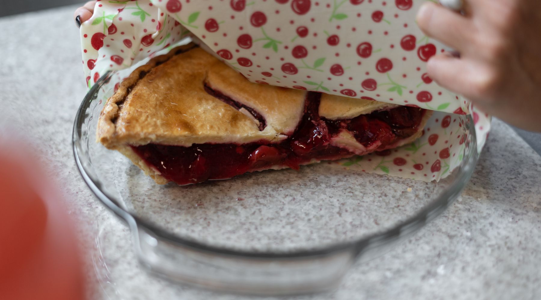 Wrapping a cherry pie in baking dish with a Good Soul Shop beeswax food wrap printed with red cherries