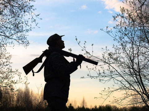 Hunter with unloaded gun looking at treestand