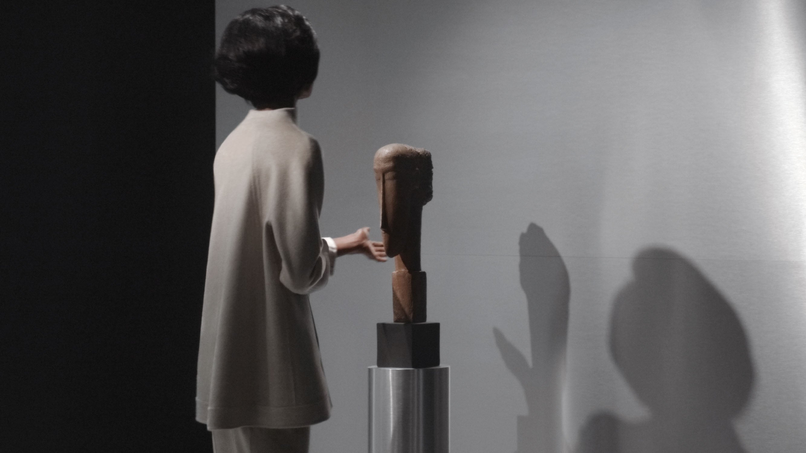 A woman touches a decorative object that is casting a shadow on the wall behind it. 