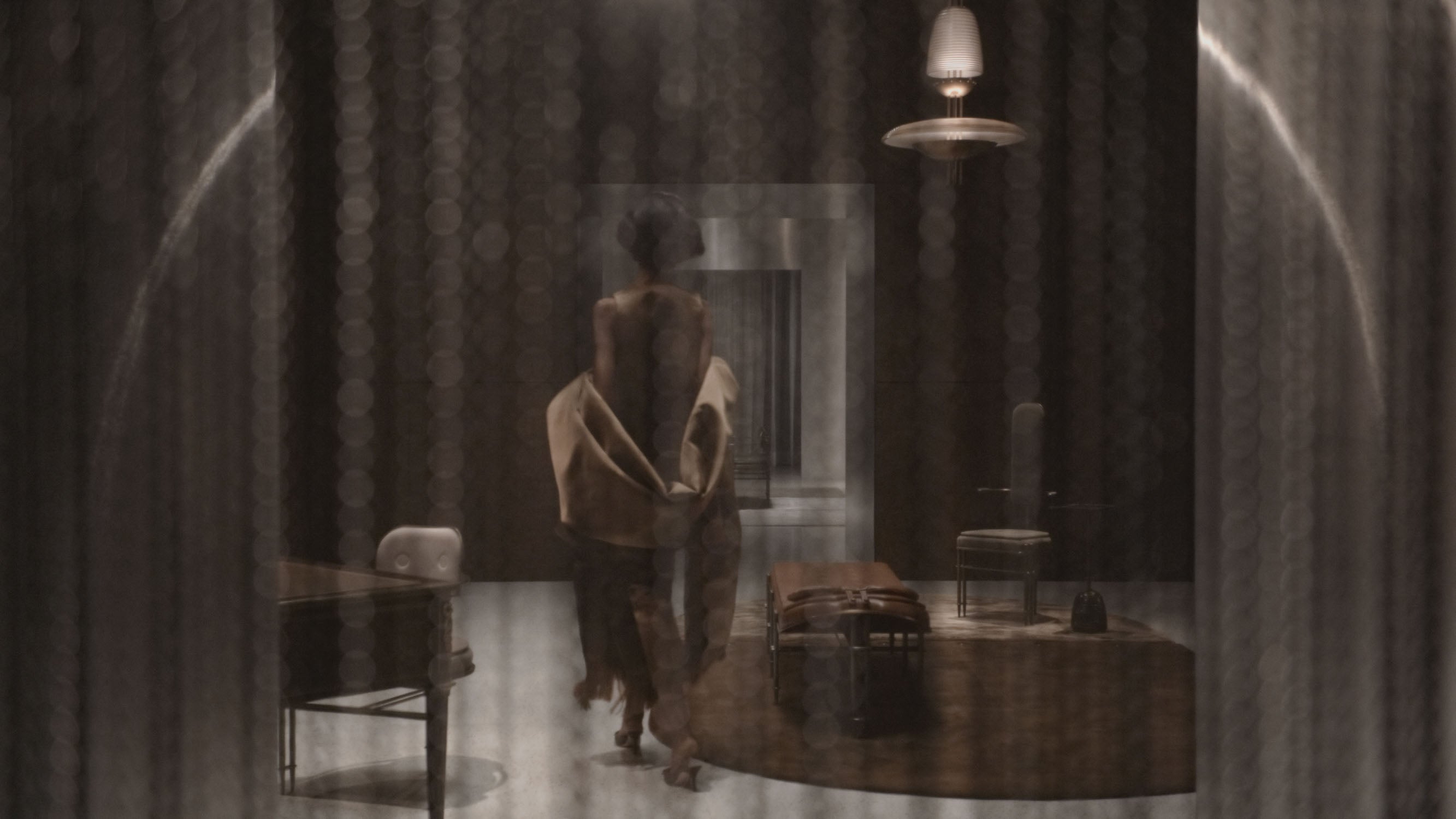 A woman walks through a room decorated with an APPARATUS ceiling pendant, chair, chaise, hall chair and modular rug. 