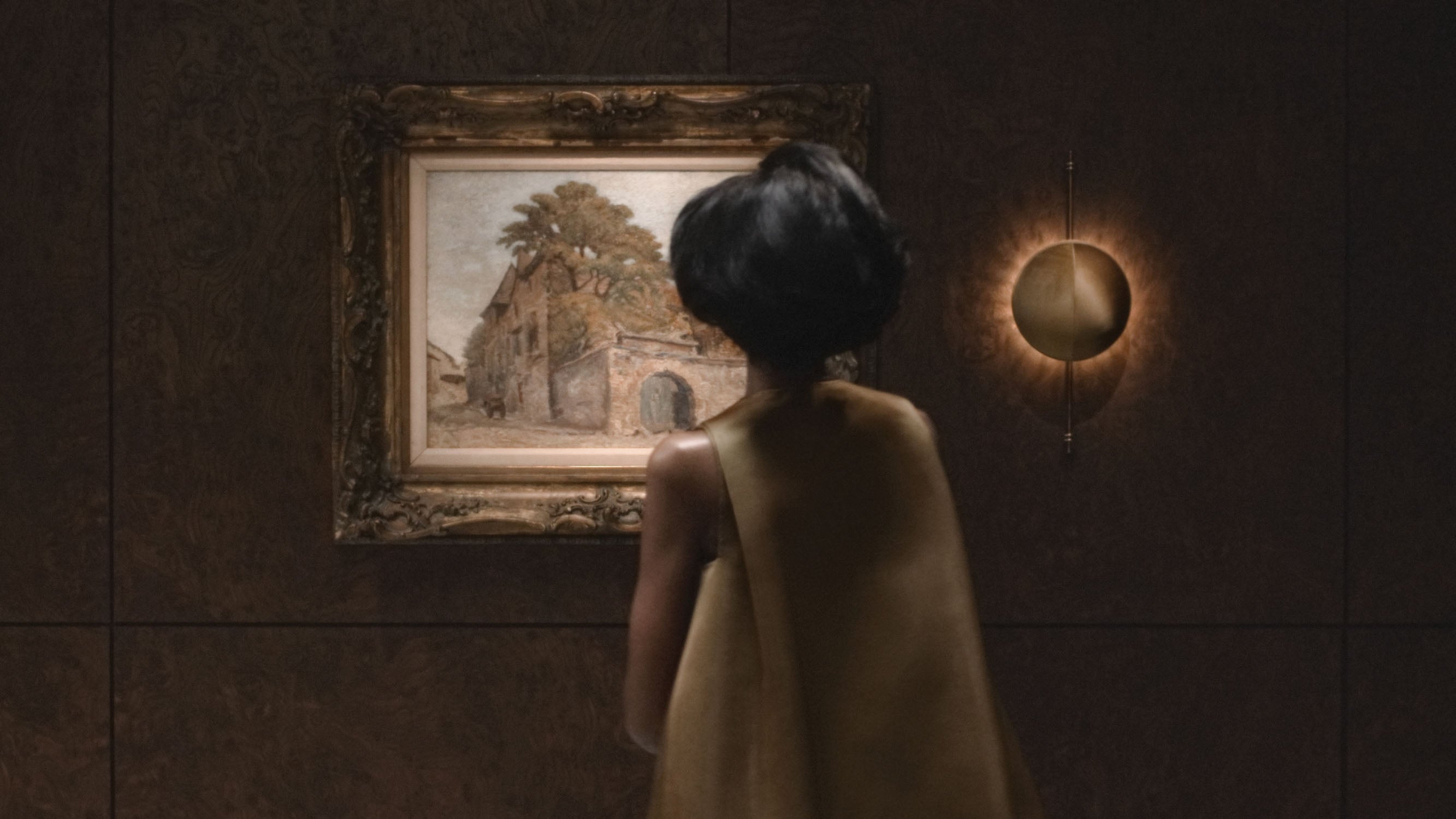 A woman admires a painting in a decorative frame that is hanging next to an illuminated STARLET wall sconce. 