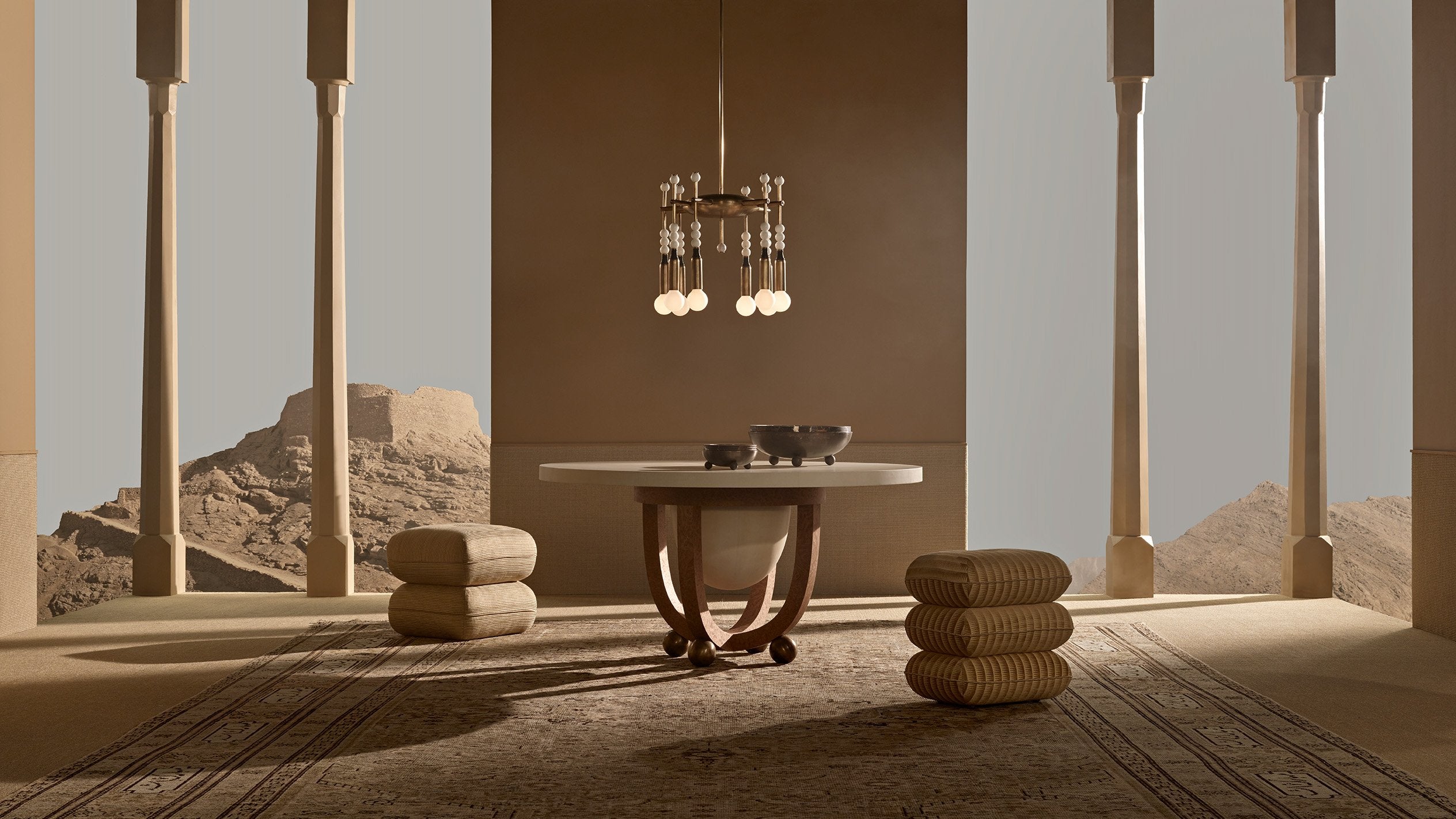 A TALISMAN : 8 chandelier hangs over a circular table on an outdoor patio with columns and a desert scene in the background. 