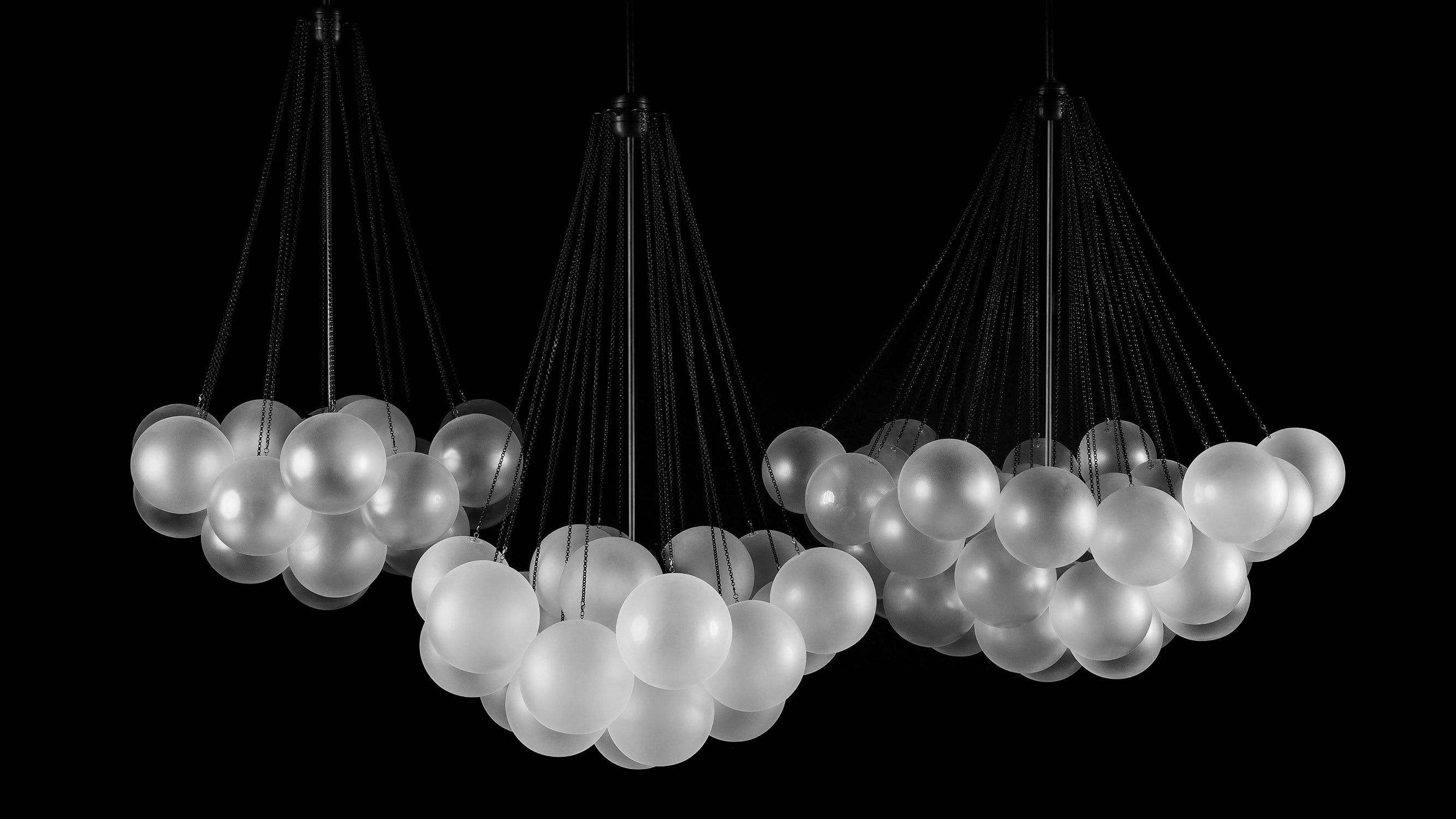 A trio of CLOUD chandeliers hanging against a black background. 
