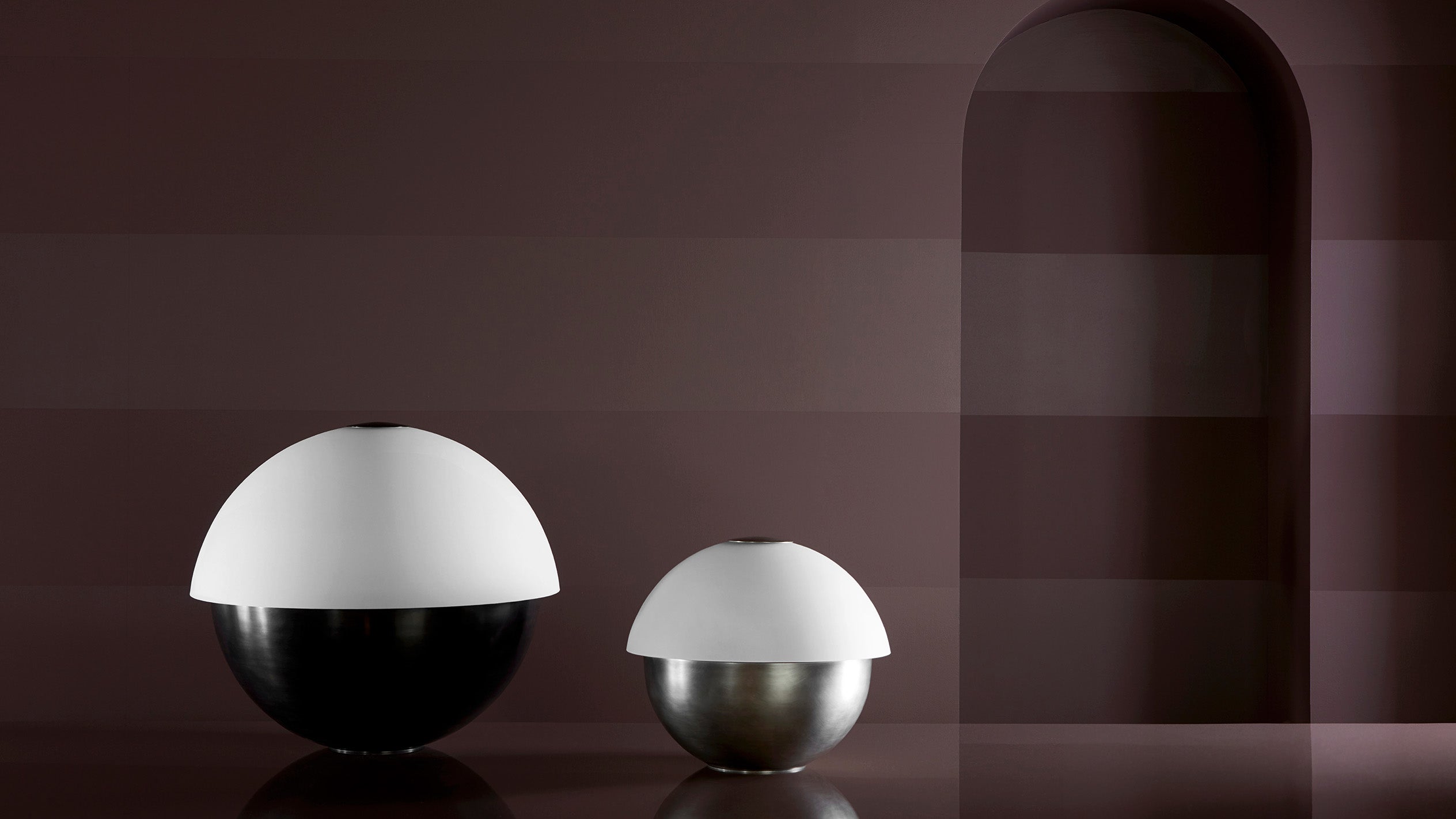 AXON : SMALL table lamp in Tarnished Silver and AXON : LARGE table lamp in Blackened Brass on a surface.