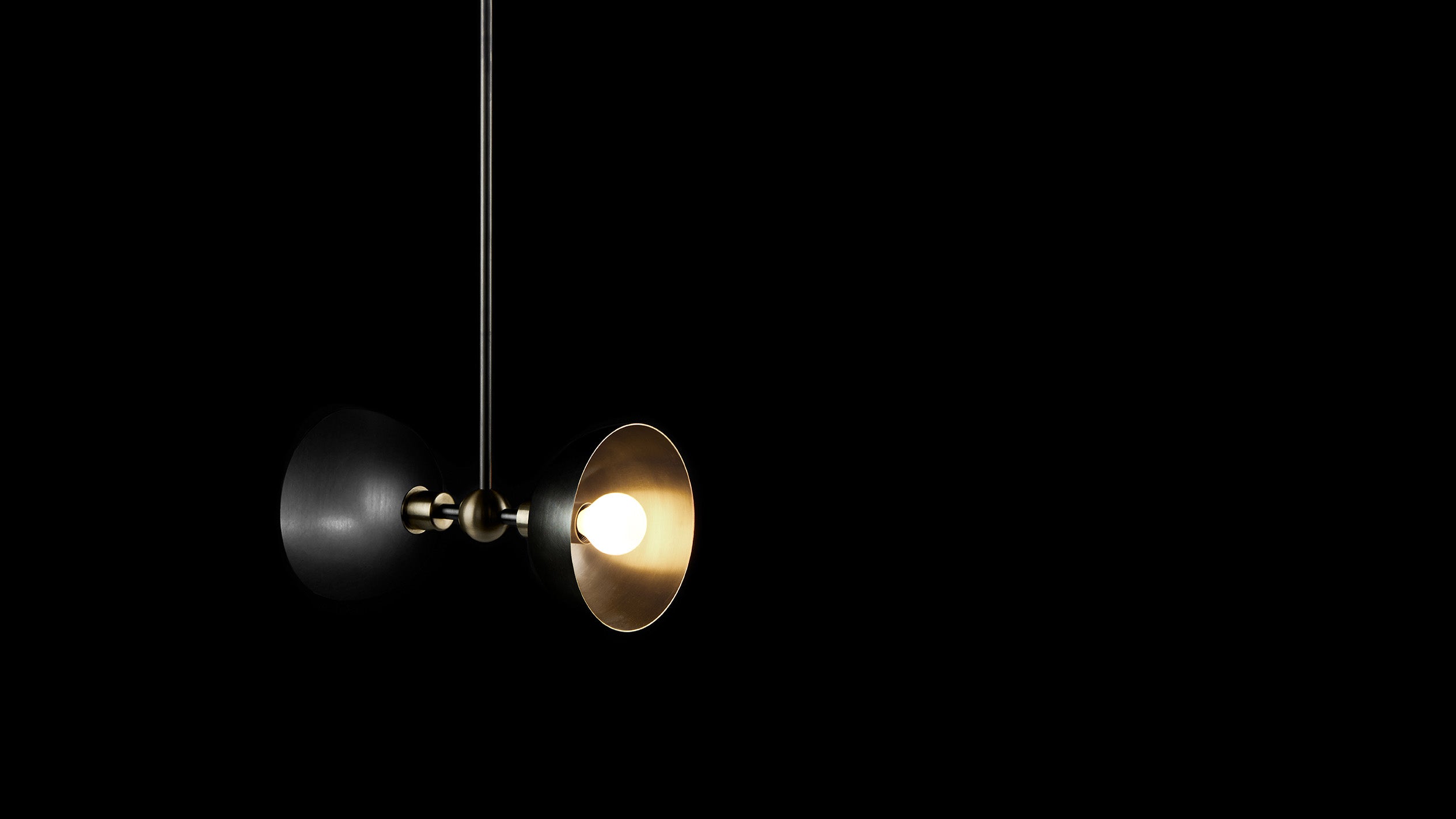 TRAPEZE : 2 ceiling pendant in Blackened Brass finish with Aged Brass bowls, hanging against a black background. 