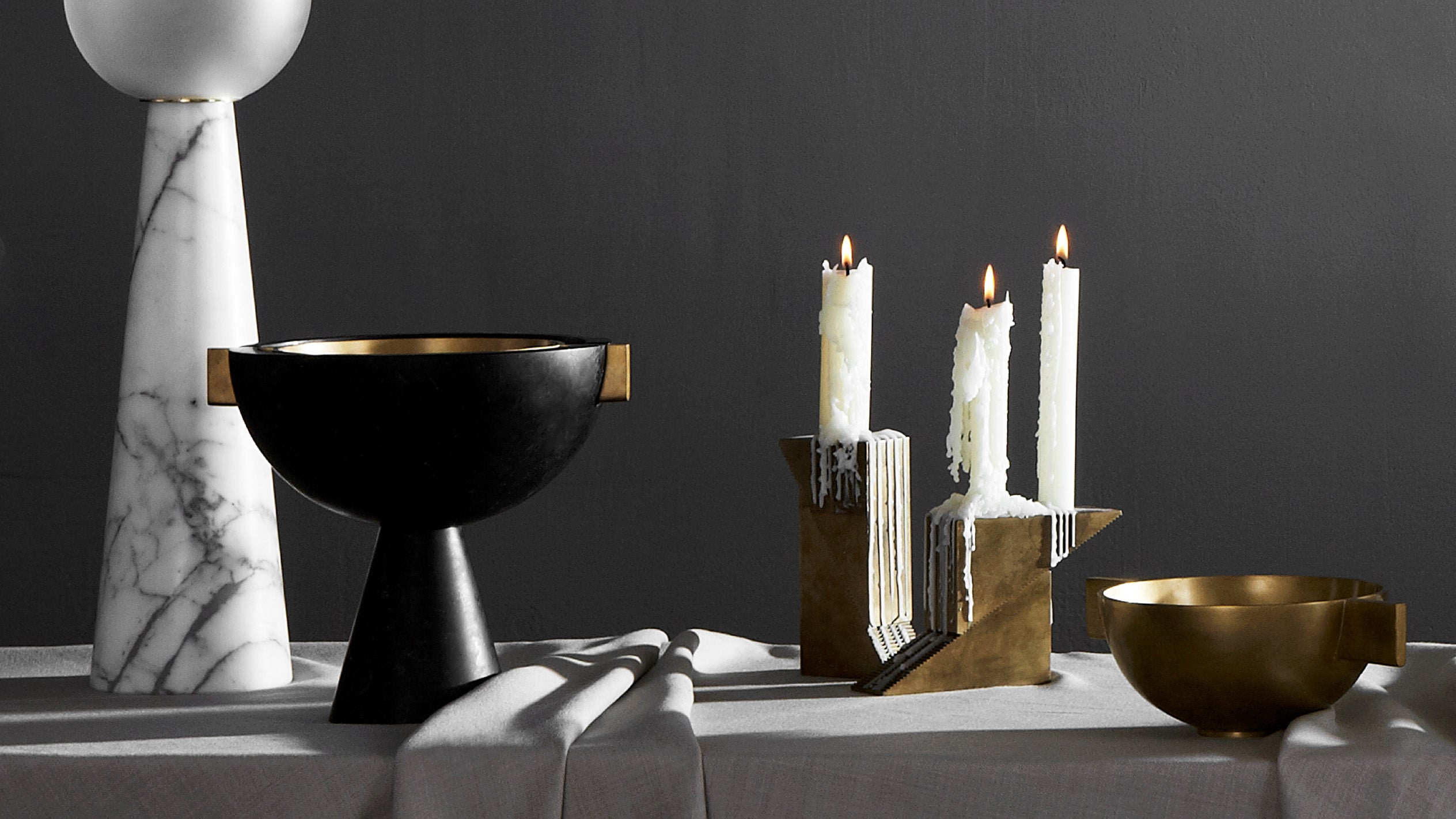 A pair of Aged Brass CANDLE BLOCKS with white candle sticks positioned on a table with other decorative objects. 