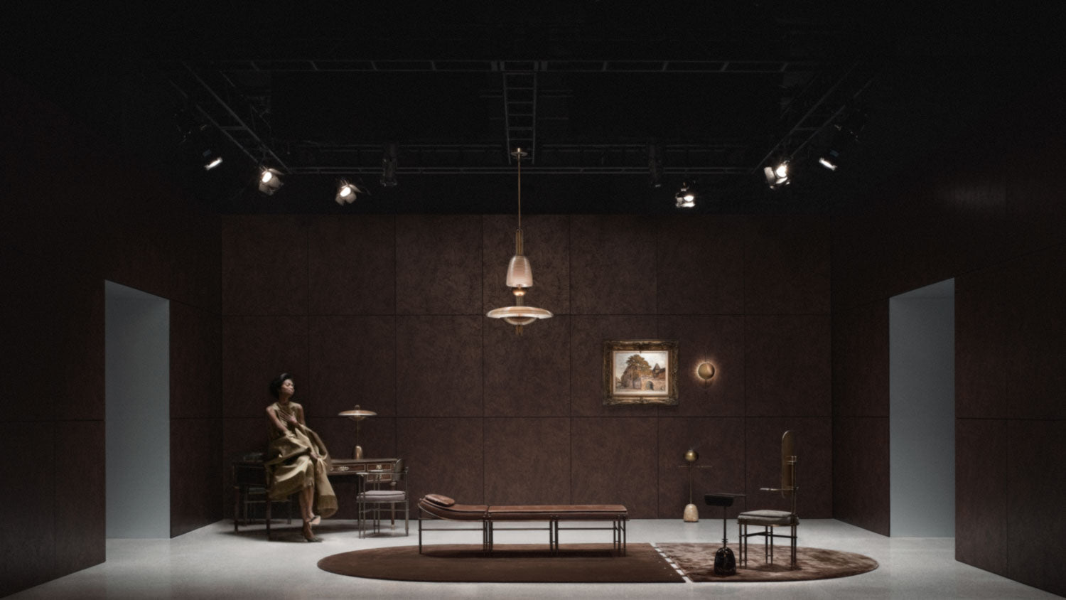 A SIGNAL : Z ceiling pendant hangs in a room above an EPISODE settee and hall chair, with a woman sitting at a desk in the background.