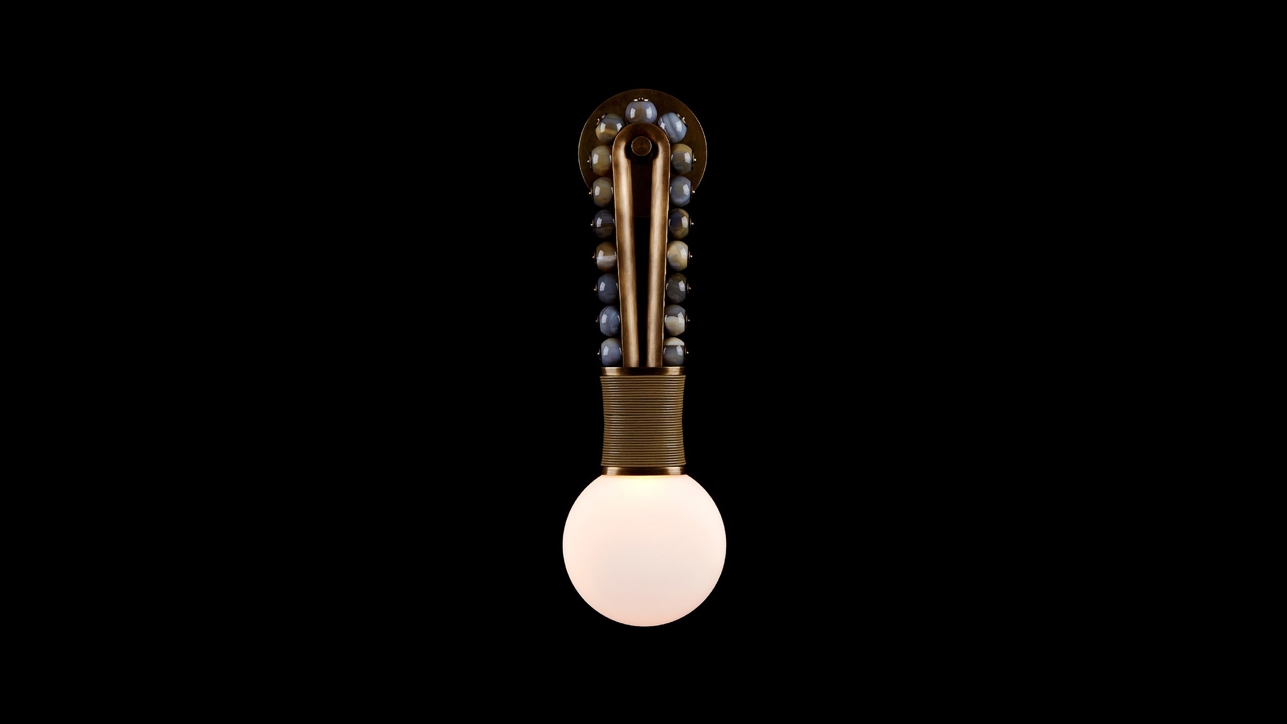 TALISMAN : LOOP sconce in Aged Brass and Tan Leather with Agate stone, mounted to a black wall. 