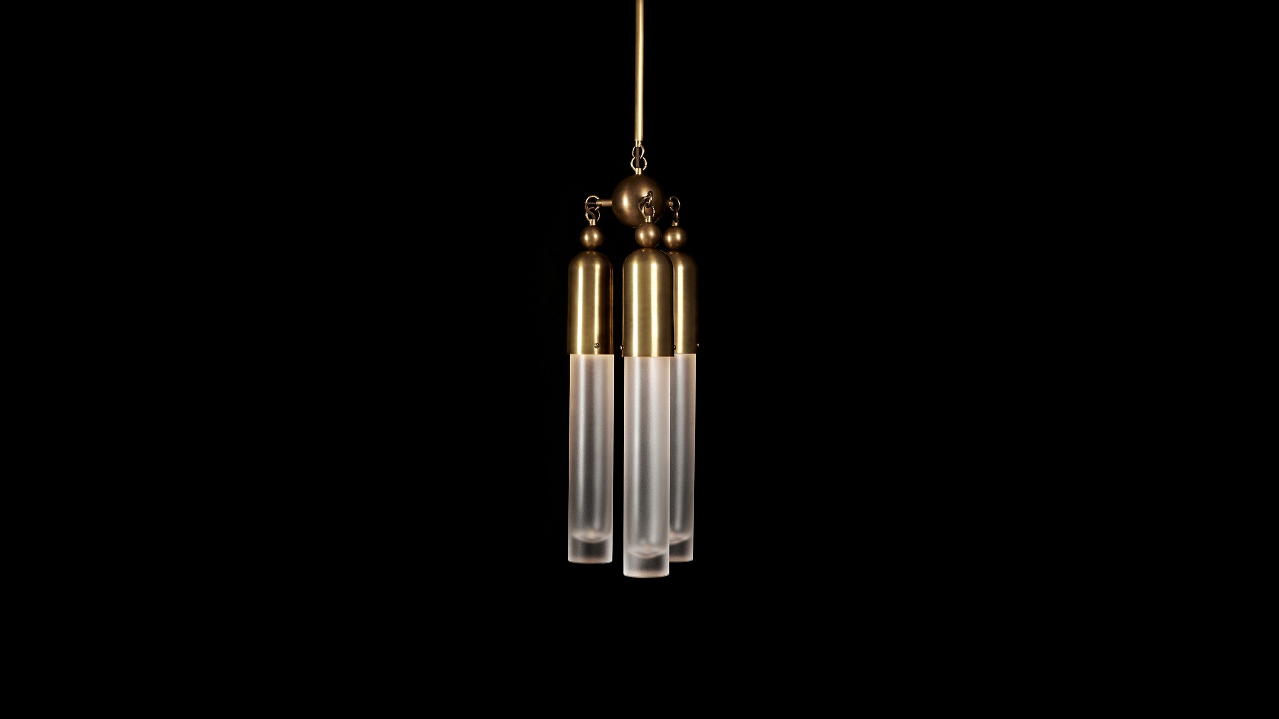 TASSEL : 3 ceiling pendant in Aged Brass finish, hanging against a black background. 
