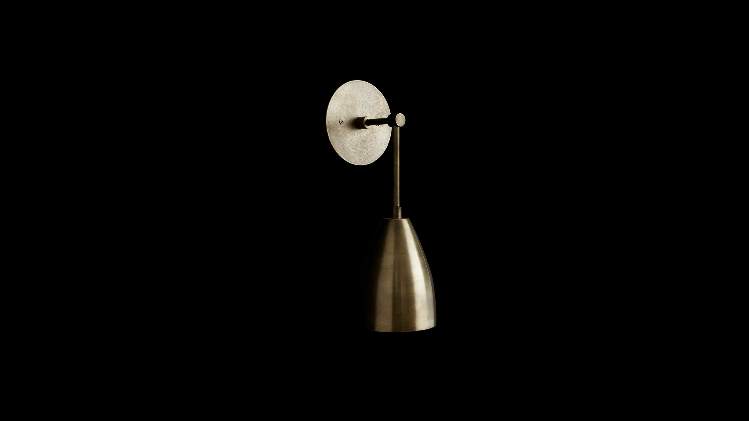 TWIG sconce in Aged Brass finish, mounted to a black wall. 