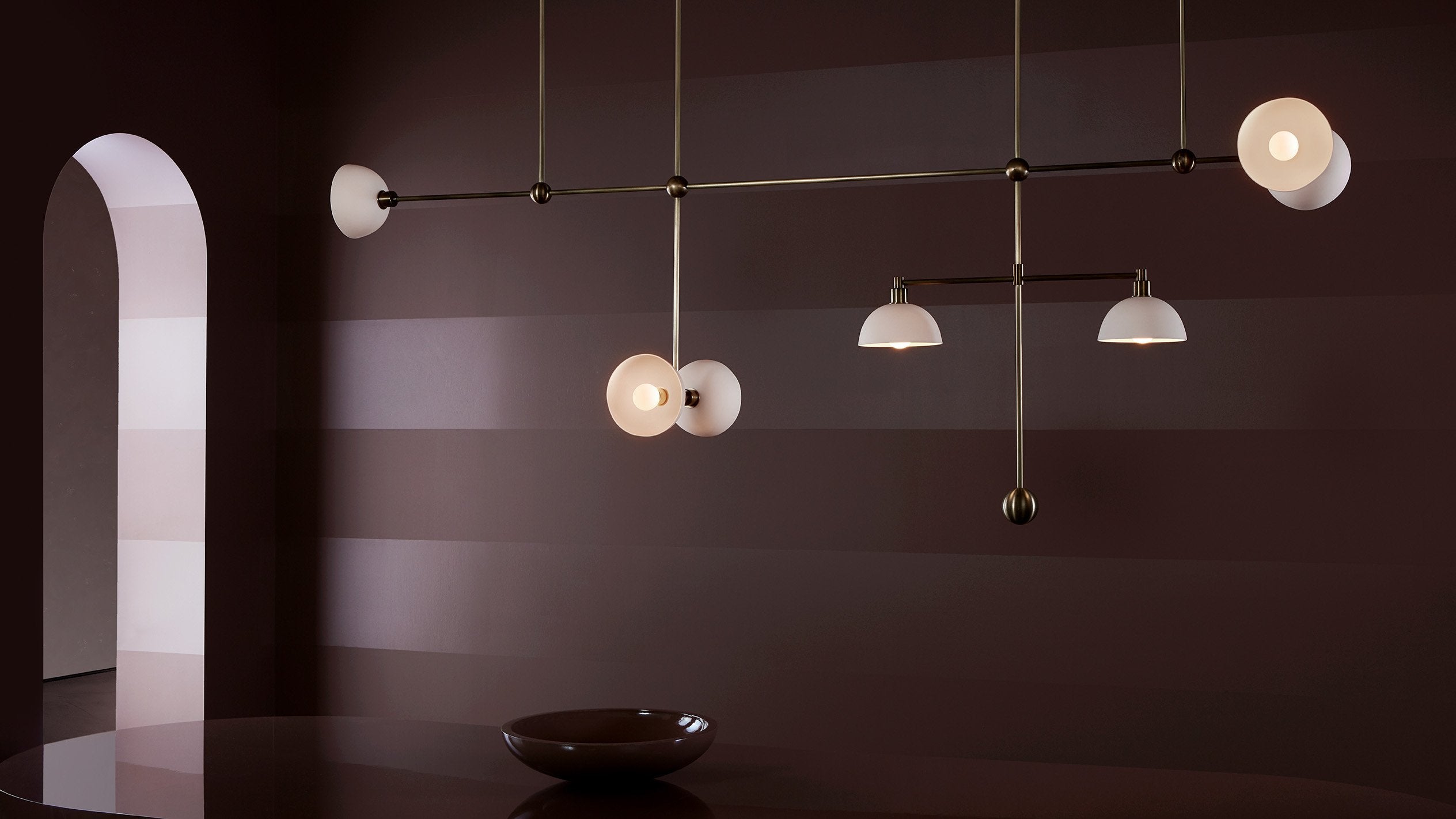 An illuminated TRAPEZE : 7 MOBILE ceiling pendant in Aged Brass with Porcelain bowls. 