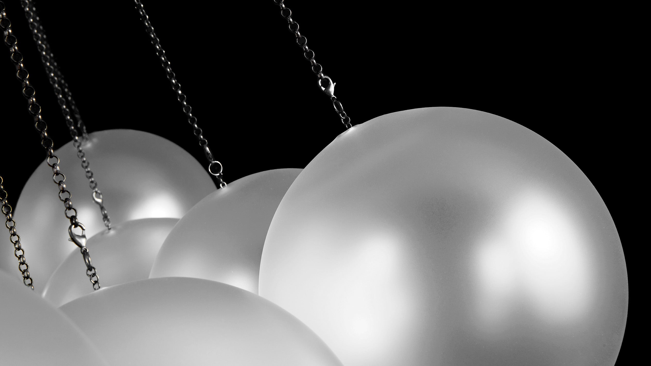 Close up of the glass orb and chain of the CLOUD chandelier in Blackened Brass finish.