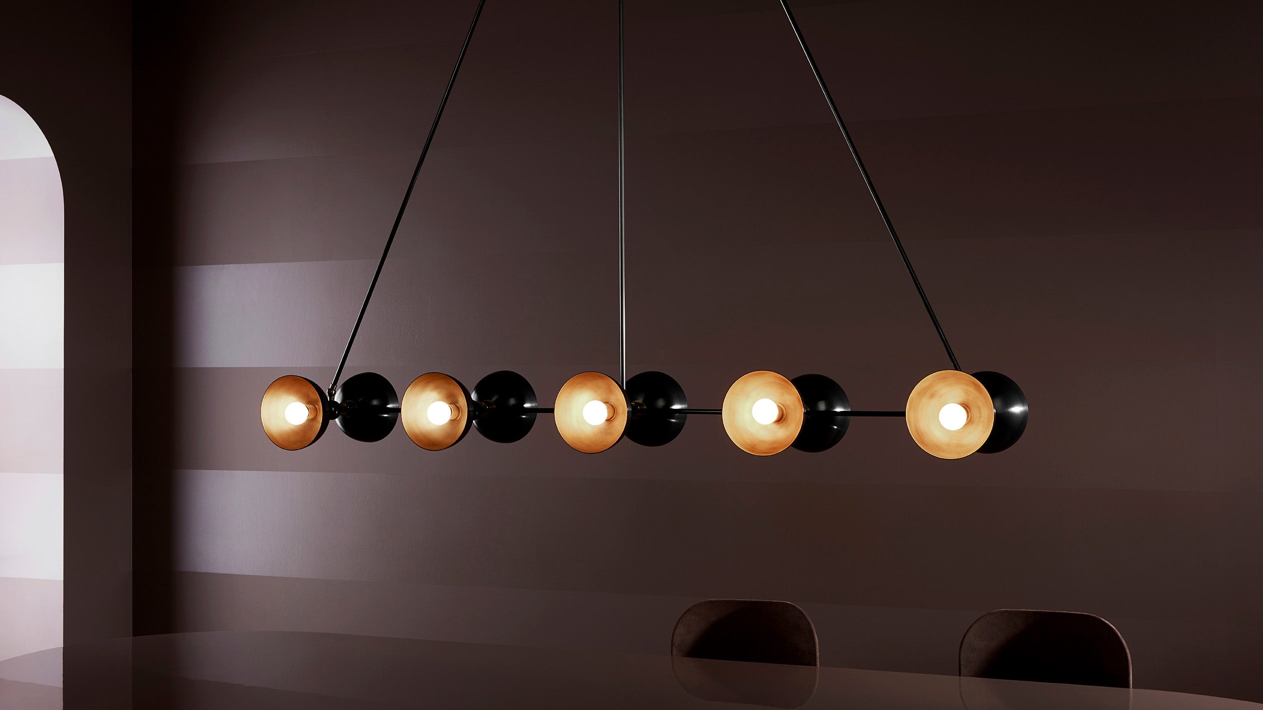 An illuminated TRAPEZE : 10 ceiling pendant in Blackened Brass finish with Aged Brass bowls. 